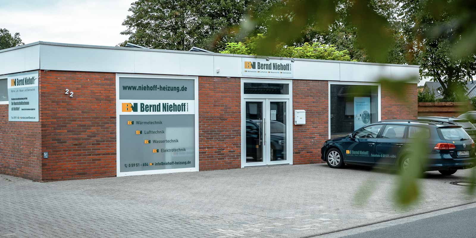 Vor dem Bürogebäude von Bernd Niehoff steht ein dunkelblauer Kombi, während die Umgebung grün und einladend wirkt.