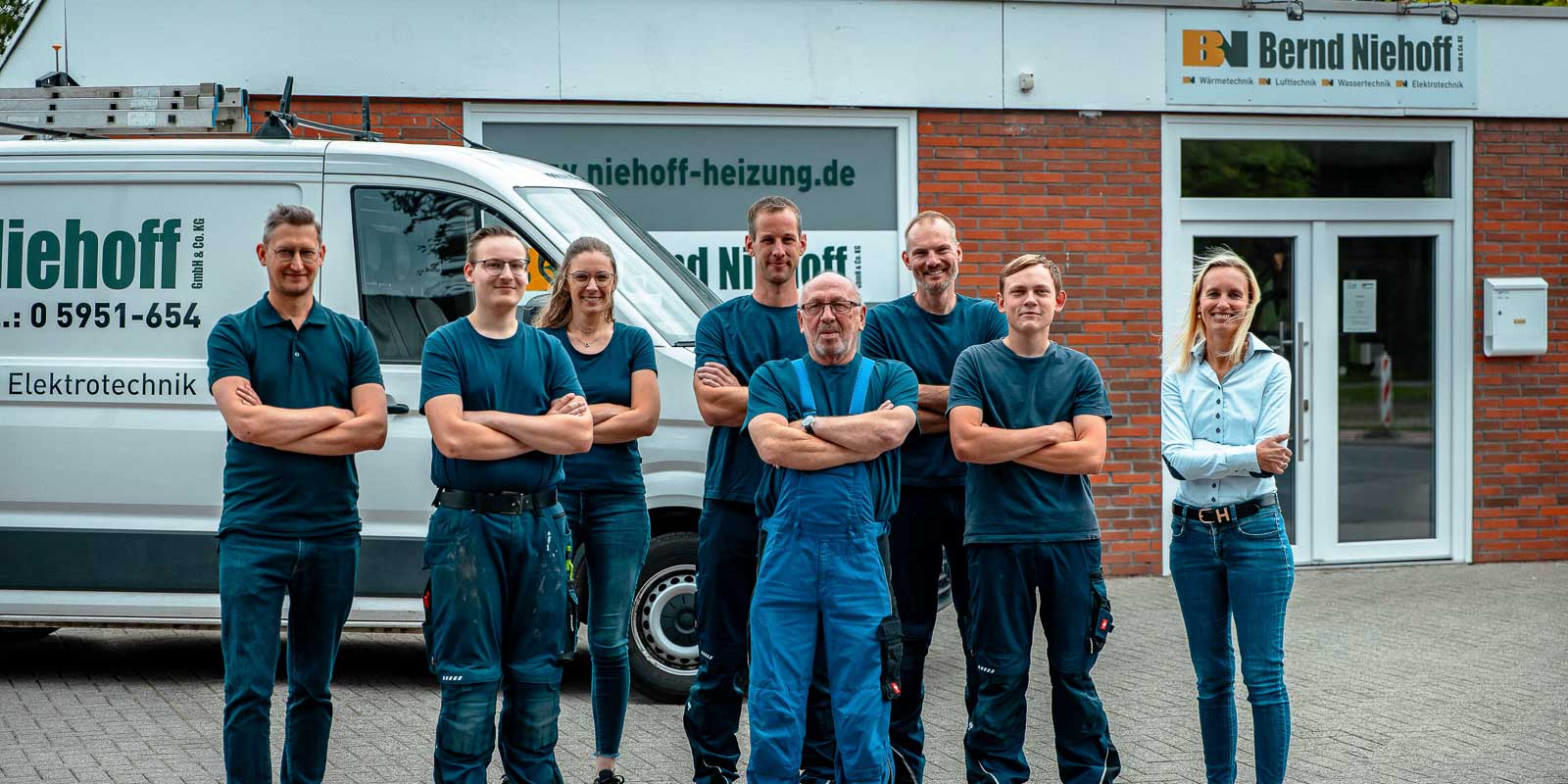 Die Mitarbeiter einer Elektrotechnik-Firma posieren stolz vor ihrem Fahrzeug, das mit dem Firmenlogo beschriftet ist.