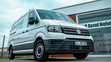 Ein moderner Lieferwagen in Weiß, der für die Firma Bernd Niehoff wirbt, steht vor einem Gebäude mit einem klaren, grauen Himmel im Hintergrund.