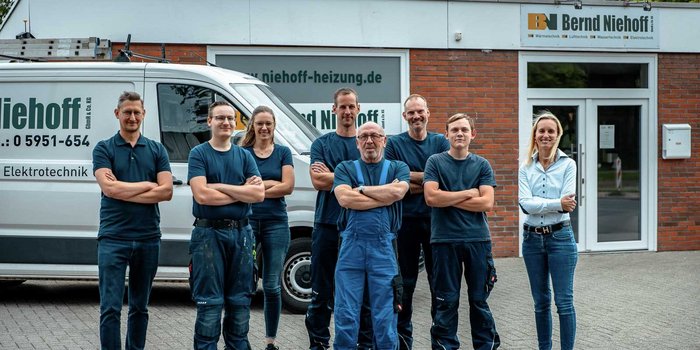 Die Teammitglieder einer Elektroinstallation-Firma zeigen Teamgeist, während sie vor ihrem Firmenfahrzeug und Büro stehen.