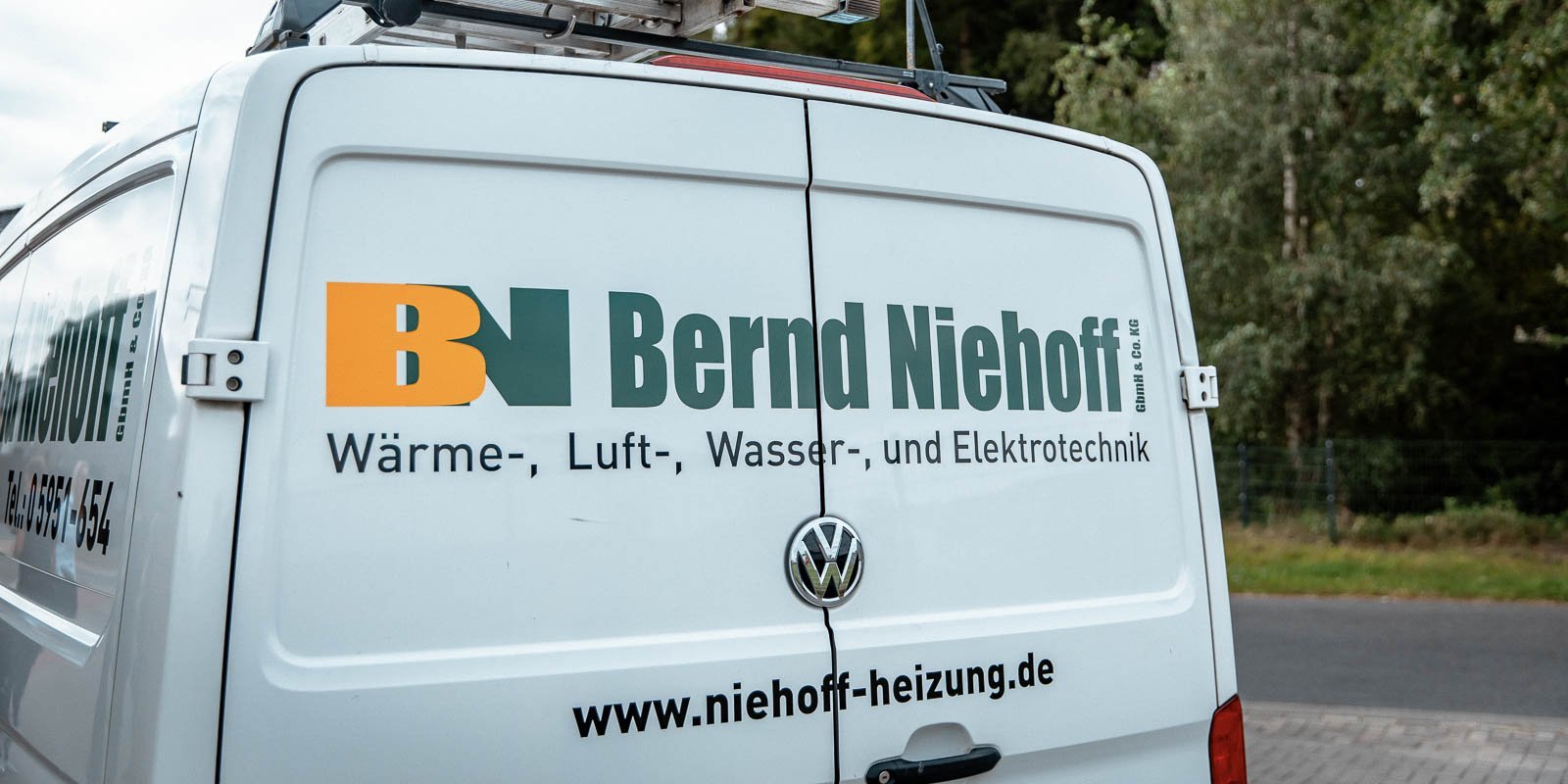 Auf der Rückseite des Fahrzeugs sind die Dienstleistungen von Bernd Niehoff deutlich sichtbar, umgeben von einer grünen Landschaft.