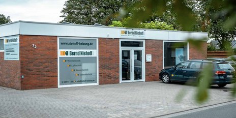 Vor dem Bürogebäude von Bernd Niehoff steht ein dunkelblauer Kombi, während die Umgebung grün und einladend wirkt.